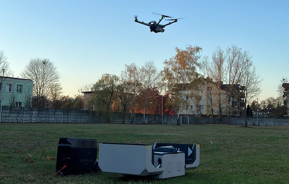 Umieszczona na trawie stacja dokująca DJI Dock 2 i lecący nad nią dron.