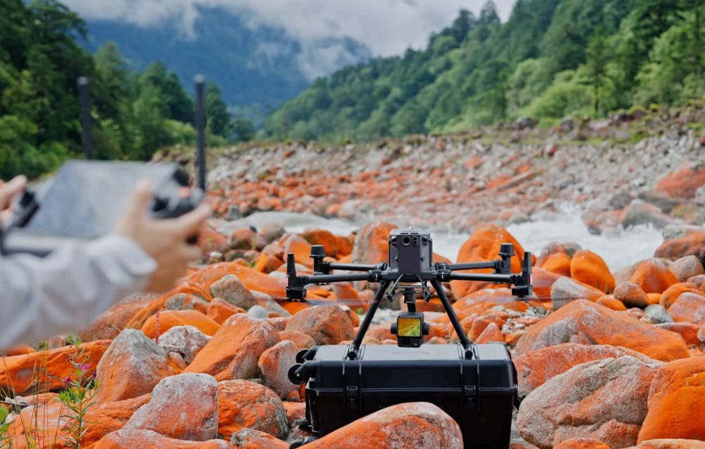 Dron DJI Matrice 350 RTK z zamontowaną kamerą Zenmuse L2 stojący na walizce transportowej ustawionej na kamieniach.